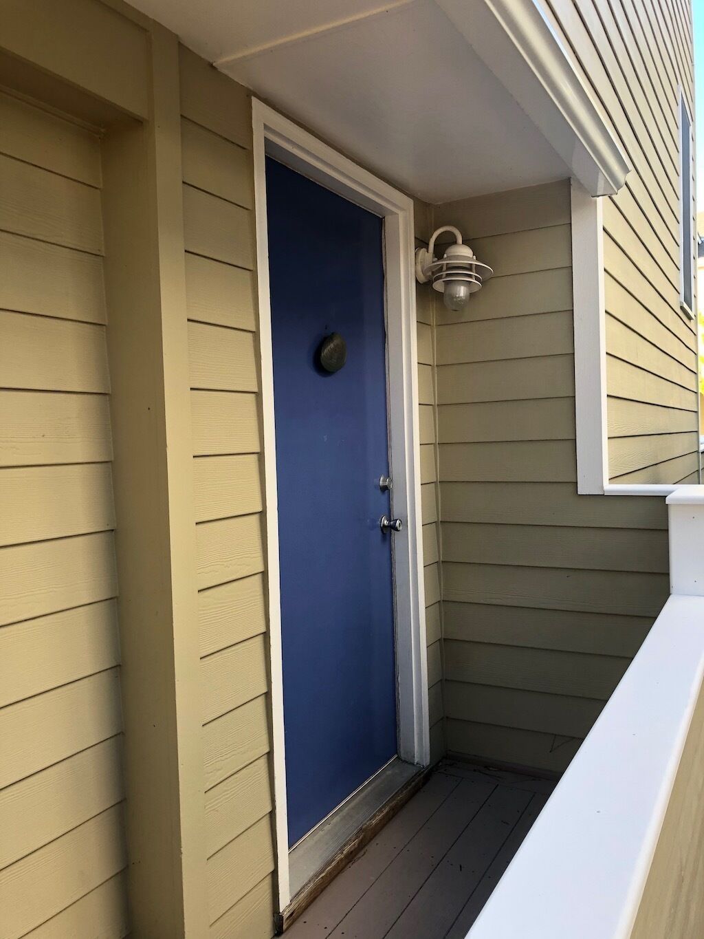 Une porte bleue avec un bouton de porte rond, des moulures blanches et un petit luminaire extérieur placé au-dessus.