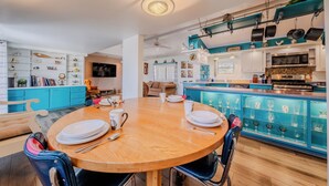 A modern kitchen with a central island, a dining area with a wooden table, and a teal accent wall. - 5 Star Comfort and Views! (Panguitch)