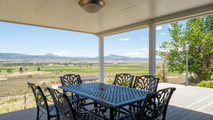 A covered outdoor patio with a table and chairs, a clock, and a view of a rural landscape with mountains. - 5 Star Comfort and Views! (Panguitch)