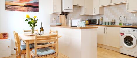 A modern kitchen with a central island, wooden chairs, a dining table, and a washing machine.