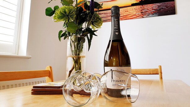 A table with a bottle of Prosecco wine, a glass, and a vase with flowers. - Little Eaton - Hidden Gem - Location by the sea with FREE parking  (Margate)