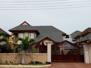 Two-story house with a gabled roof, set behind a stone wall and gated entrance.