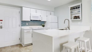 A modern kitchen with white cabinetry, a central island with stools, a microwave, and a refrigerator.