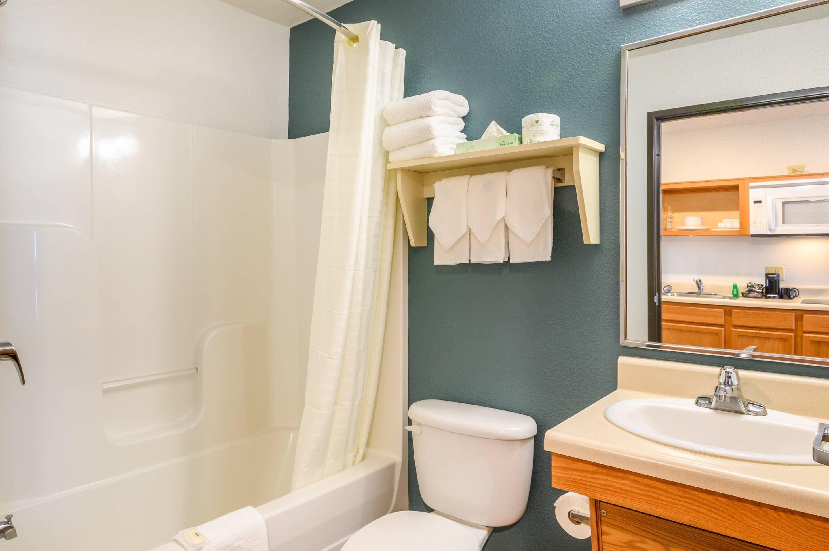 A bathroom with a bathtub, toilet, sink, and a shelf with towels.