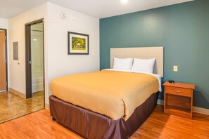 Une chambre d’hôtel avec un lit, une table de chevet, un tableau encadré au mur et une porte sur le côté gauche.