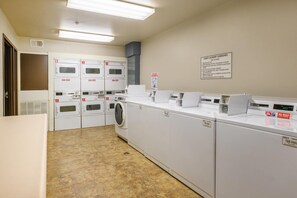 En tvättstuga på hotellet med flera tvättmaskiner och torktumlare, en skylt med information om hur gästerna får använda tvättstugan samt ett ventilationssystem i taket.