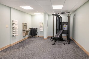 A fitness room with a bench press, a squat rack, and a water dispenser. - Suburban Studios Hammond (Hammond)