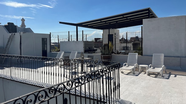 Eine Dachterrasse mit weißen Liegestühlen, einem Metallgeländer und Blick auf die Stadtlandschaft.