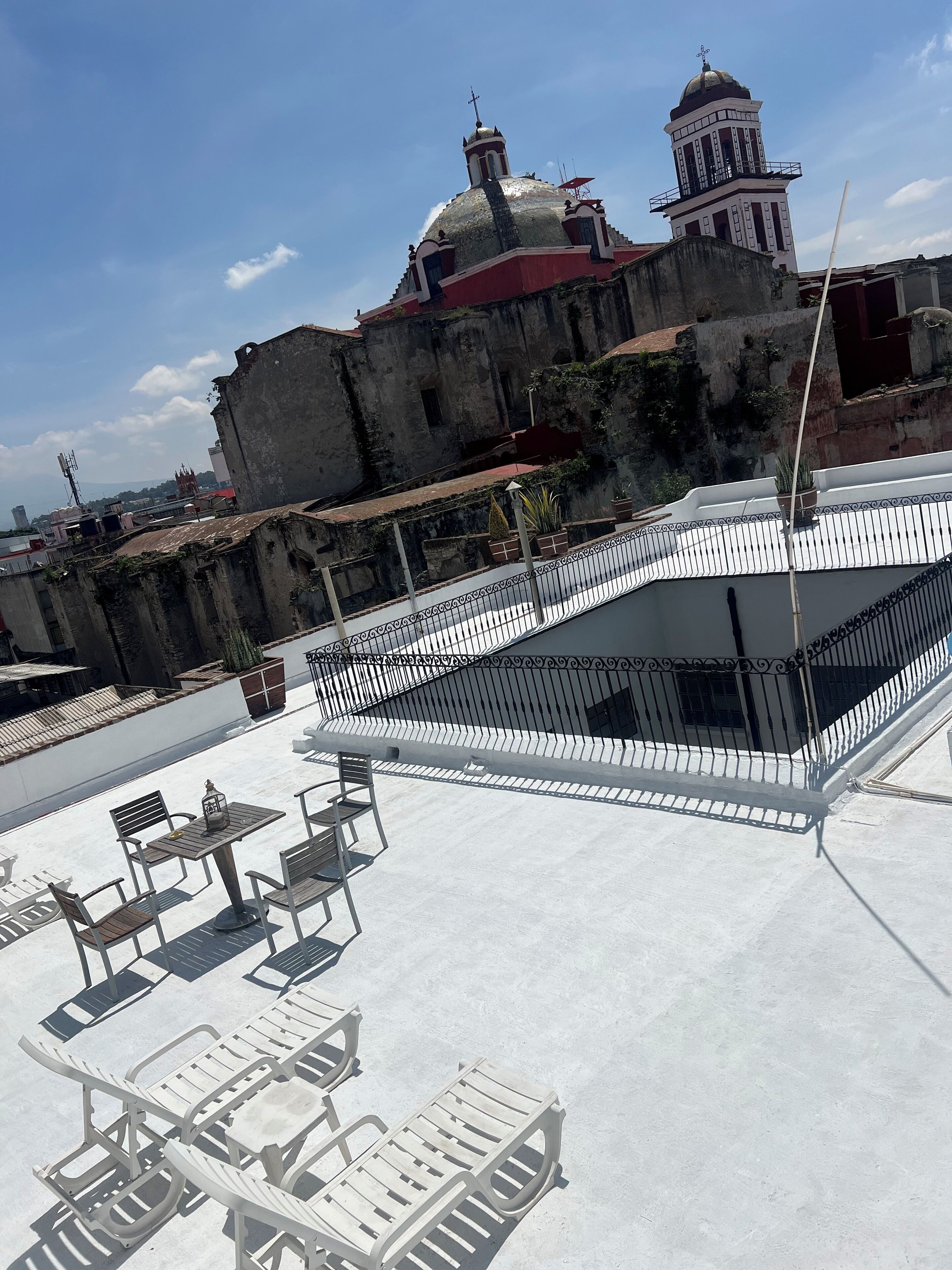 Una terraza en la azotea con mobiliario exterior y vistas a un edificio histórico con cúpula y campanario.