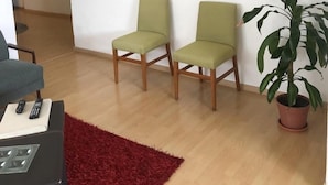 Ein Wohnzimmer mit zwei grünen Sesseln, einem roten Teppich, einer Topfpflanze und einem Wandbild.