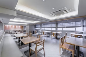 A modern dining area with multiple tables and chairs, large windows, and a skylight. - JI Hotel (Shanghai)