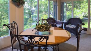 A sunroom with a round wooden table, black metal chairs, and a view of greenery outside. - Walk-In Condo With Pools in Pointe Royale - 2 Kings - Sleeps 6 (Branson)