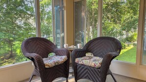 Two wicker chairs with patterned cushions, a small table with a cup and saucer, and a view of a green landscape through large windows. - Walk-In Condo With Pools in Pointe Royale - 2 Kings - Sleeps 6 (Branson)