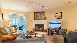 A living room with a fireplace, a television, leather sofas, and a dining area. - Walk-In Condo With Pools in Pointe Royale - 2 Kings - Sleeps 6 (Branson)
