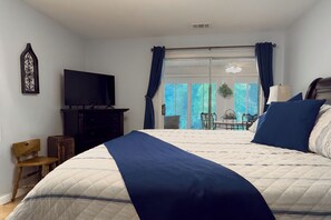 A bedroom with a bed, a television, a chair, and a view of the outdoors through a sliding door. - Walk-In Condo With Pools in Pointe Royale - 2 Kings - Sleeps 6 (Branson)