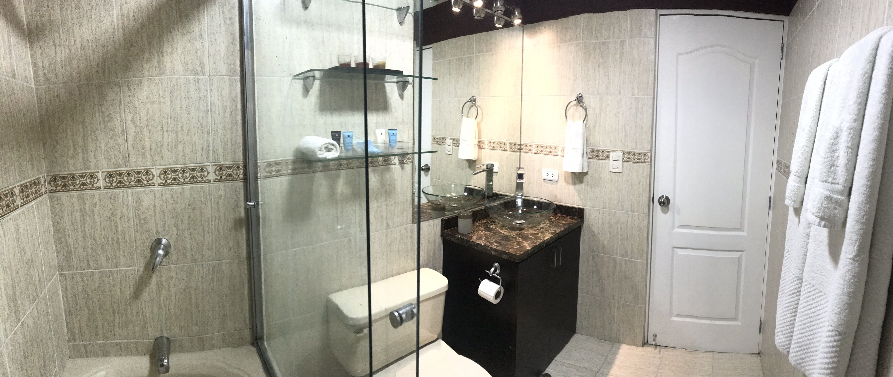 A modern bathroom with a glass-enclosed shower, a black vanity with a glass bowl sink, and a white door.