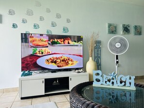 A living room with a flat-screen TV, a decorative wall with fish decals, a fan, and a 'Beach' sign.