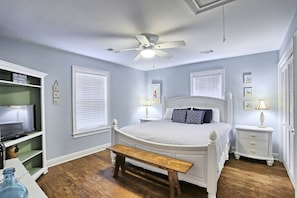 A bedroom with a bed, a ceiling fan, a bench, bedside tables, a TV, and a shelf.