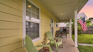 A covered porch with green chairs, a table, and an American flag. - Pet-Friendly | Steps to Beach & Old Town BSL! (Bay St. Louis)