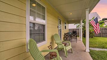 A covered porch with green chairs, a table, and an American flag.