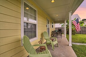 A covered porch with green chairs, a table, and an American flag.