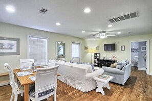 A spacious living area with a dining table, two sofas, a TV, and a ceiling fan.