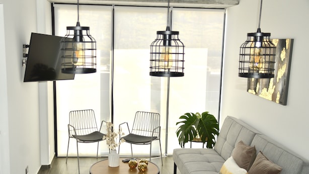 A modern living room with a grey sofa, two black chairs, a round coffee table with decorative items, and a large window with natural light. - Cozy Stays Cayala Apartments 3 (Guatemala)