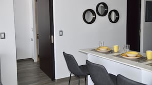A modern dining area with a white table, black chairs, and a wall-mounted mirror. - Cozy Stays Cayala Apartments 3 (Guatemala)