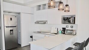 A modern kitchen with a stainless steel refrigerator, a microwave, a toaster, and a large island with bar stools. - Cozy Stays Cayala Apartments 3 (Guatemala)
