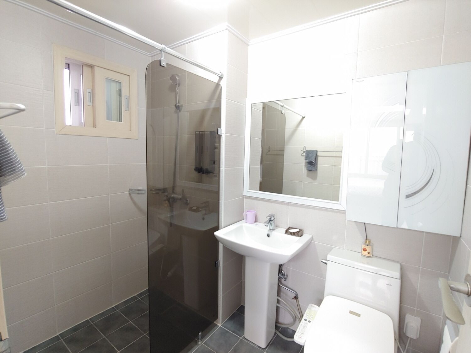 A modern bathroom with a glass shower enclosure, a pedestal sink, and a toilet.