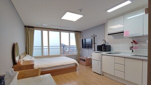 Ein modernes Hotelzimmer mit Bett, einer kleinen Küchenzeile, einem Fernseher und einem Balkon mit Blick.