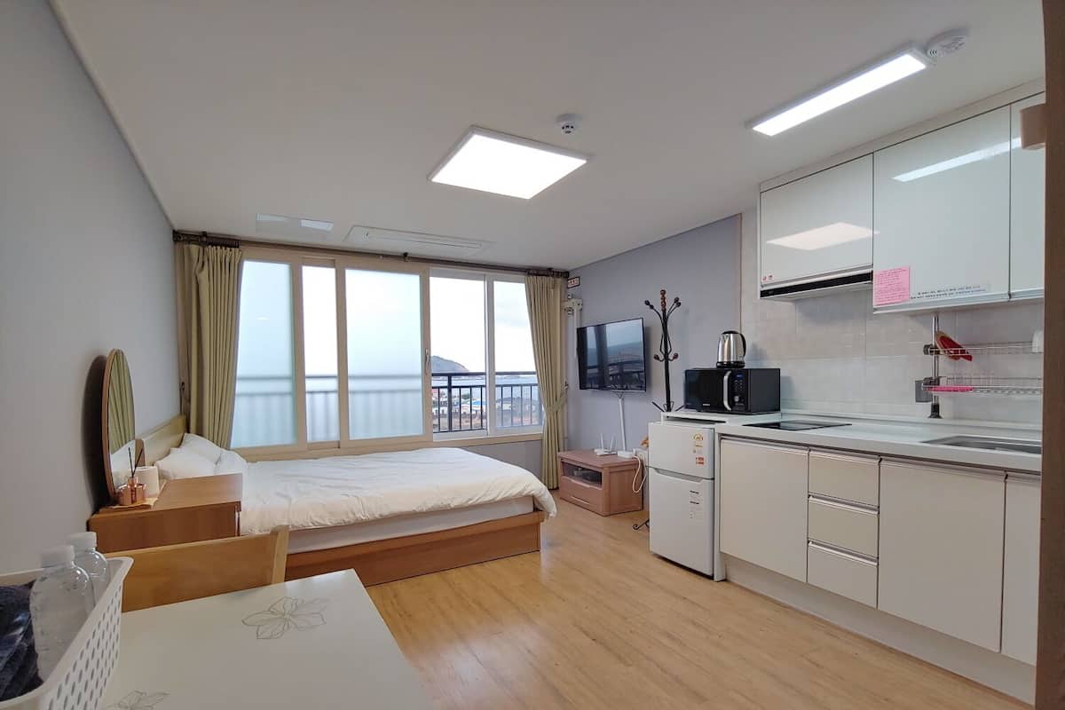 Ein modernes Hotelzimmer mit Bett, einer kleinen Küchenzeile, einem Fernseher und einem Balkon mit Blick.