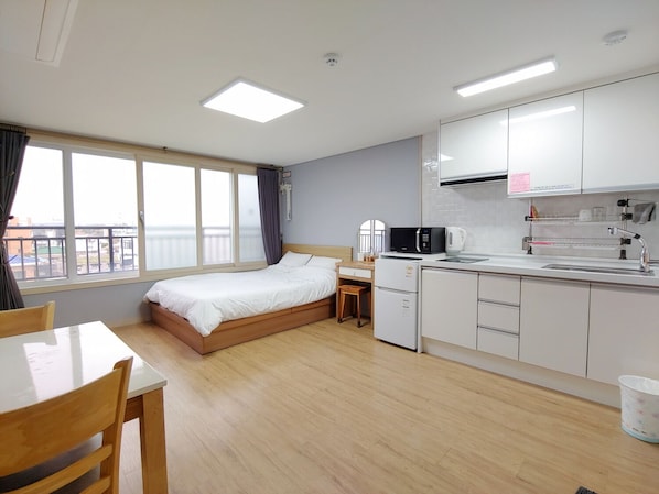Habitación de hotel con cama, escritorio, kitchenette y ventana con cortinas.