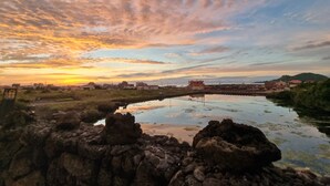 Ein Sonnenuntergang über ruhigem Wasser, im Vordergrund Felsformationen.