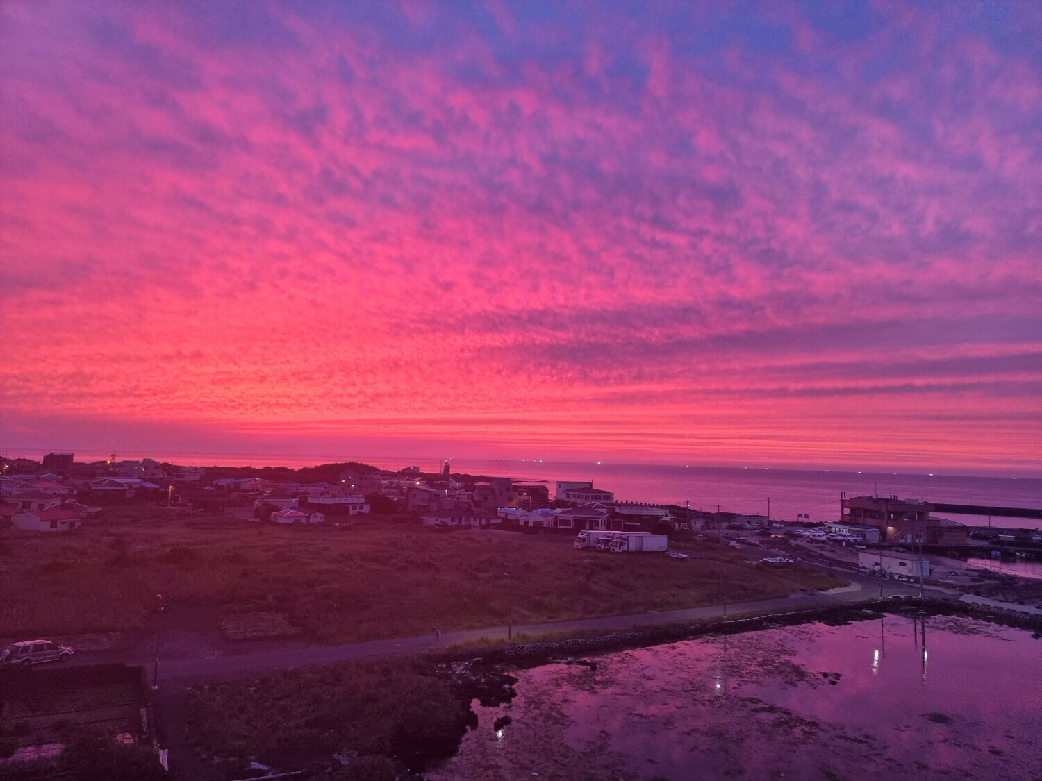 A coastal town at sunset with buildings and a waterfront.