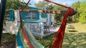 A hammock tied to a wooden structure with a view of a house and a trampoline in the background. - A garden oasis for the nature lover who likes modern comforts (Gregory Town)