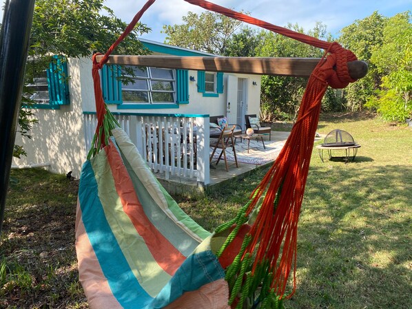 Un hamac est attaché à une structure en bois, d’où l’on aperçoit une maison et, au loin, un trampoline.