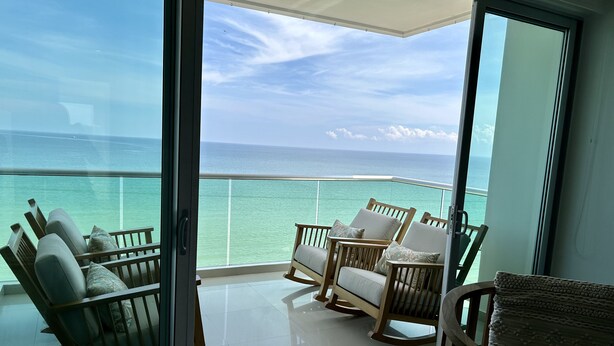 A balcony with a glass door, wooden rocking chairs, and a view of the ocean.