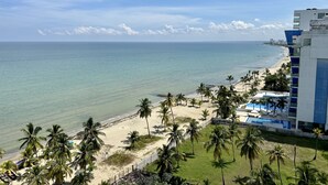 A beachfront hotel with a pool, palm trees, and a view of the ocean.