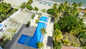 A resort with a large swimming pool, a beach, and palm trees.