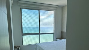 A bedroom with a large window, a bed, a bedside table, and a small wicker basket.