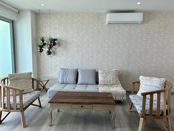 A modern living room with a sofa, two wooden chairs, a wooden coffee table, and a patterned wall.