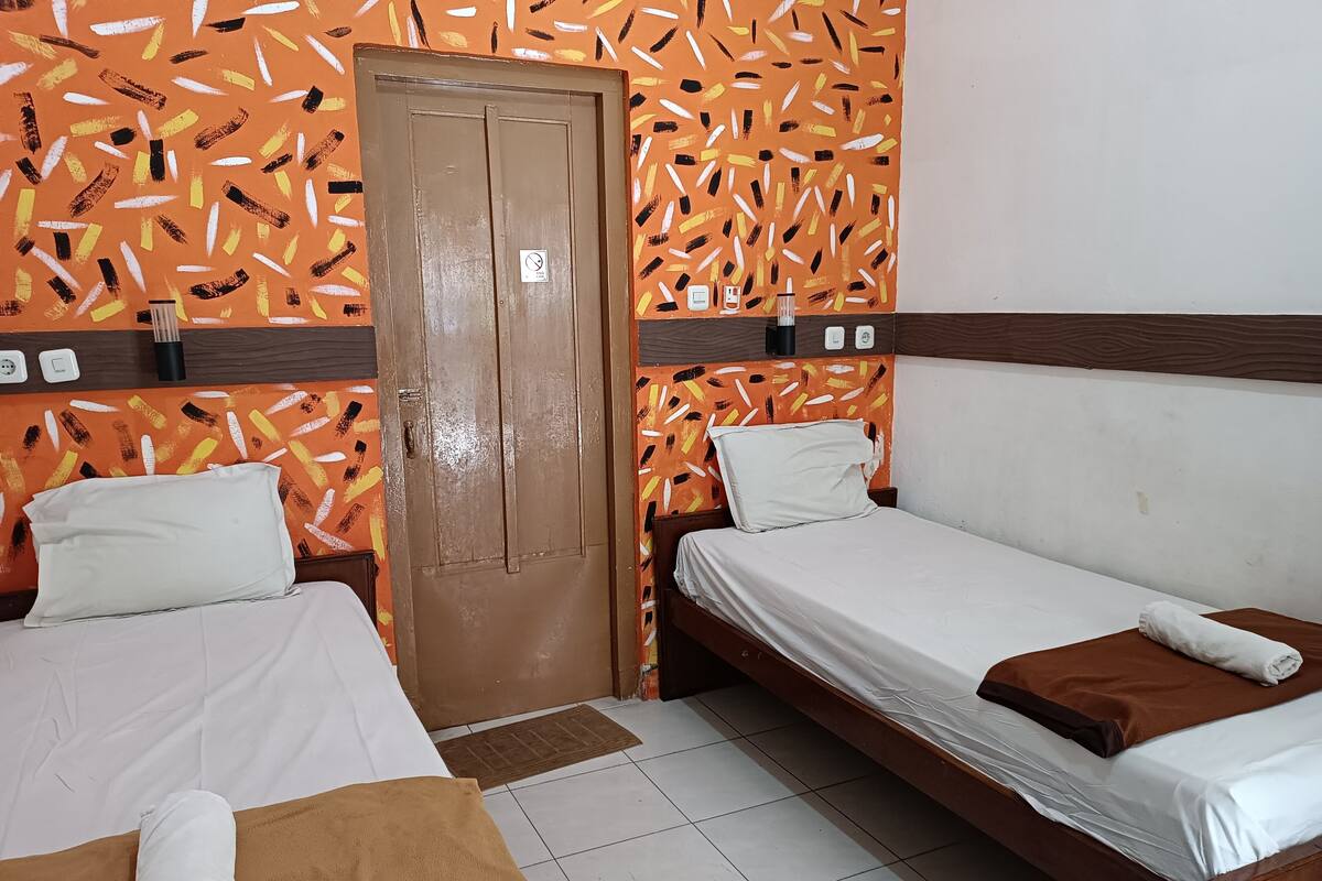 A hotel room with two single beds, a wooden door, and a patterned orange wall.