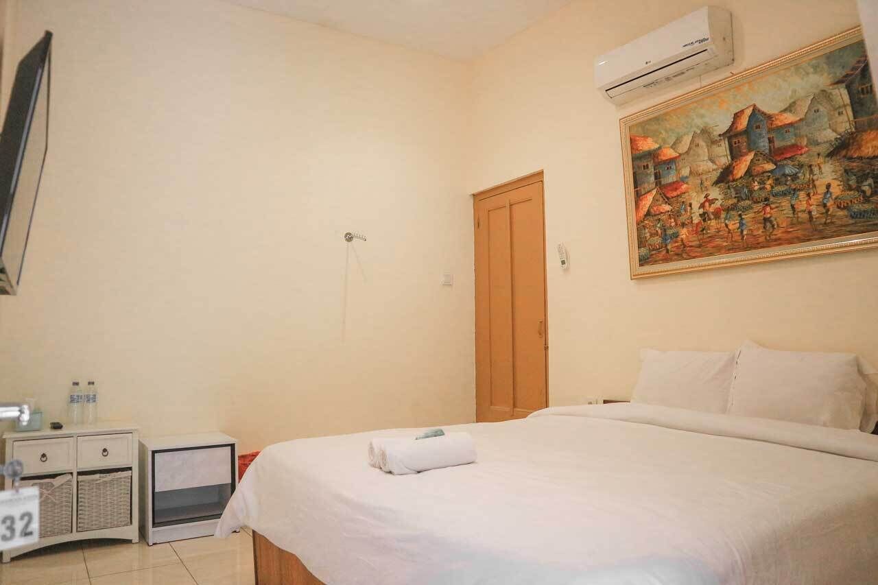 A hotel room with a bed, a nightstand, a wall-mounted air conditioner, and a painting.