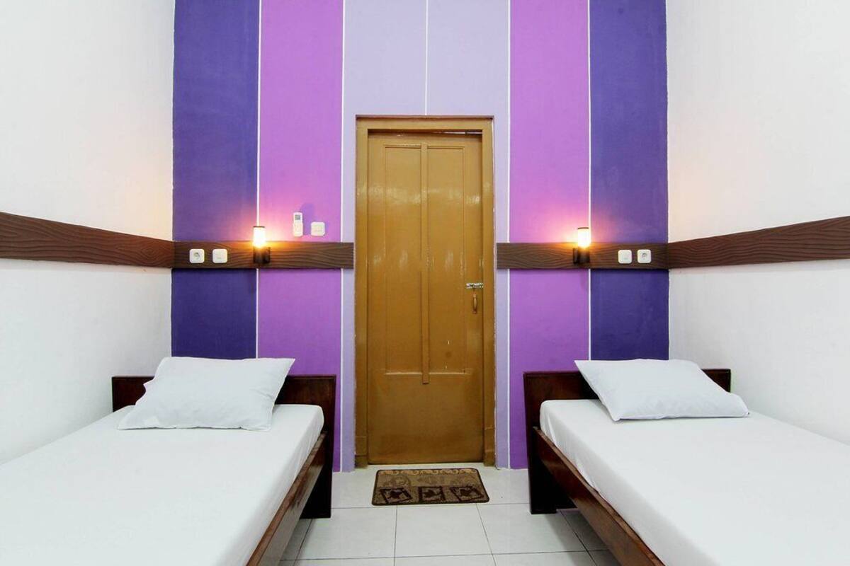 A room with two single beds, a wooden door, and purple and white walls.