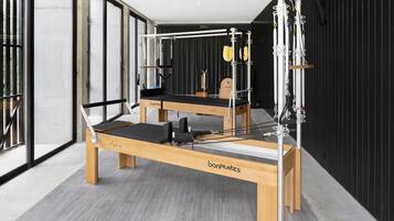 Pilates-studio, jossa on kaksi puista reformer-laitetta, musta jumppamatto ja puinen penkki.