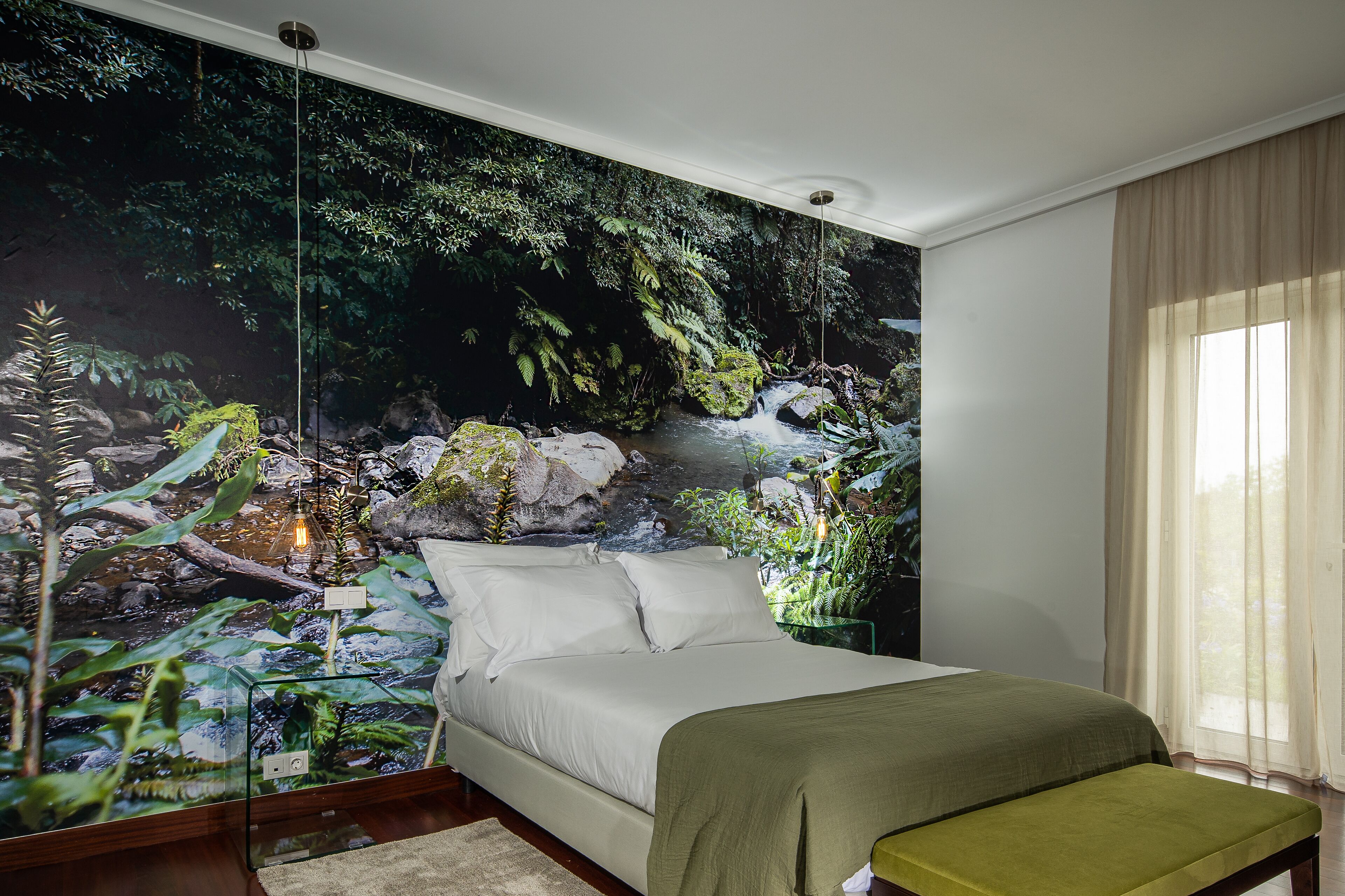 A bedroom with a large mural of a forest scene, a bed with white linens, and a bench.