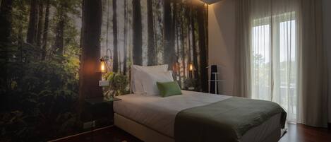 A bedroom with a large bed, a nightstand, a lamp, and a wall mural of a forest.