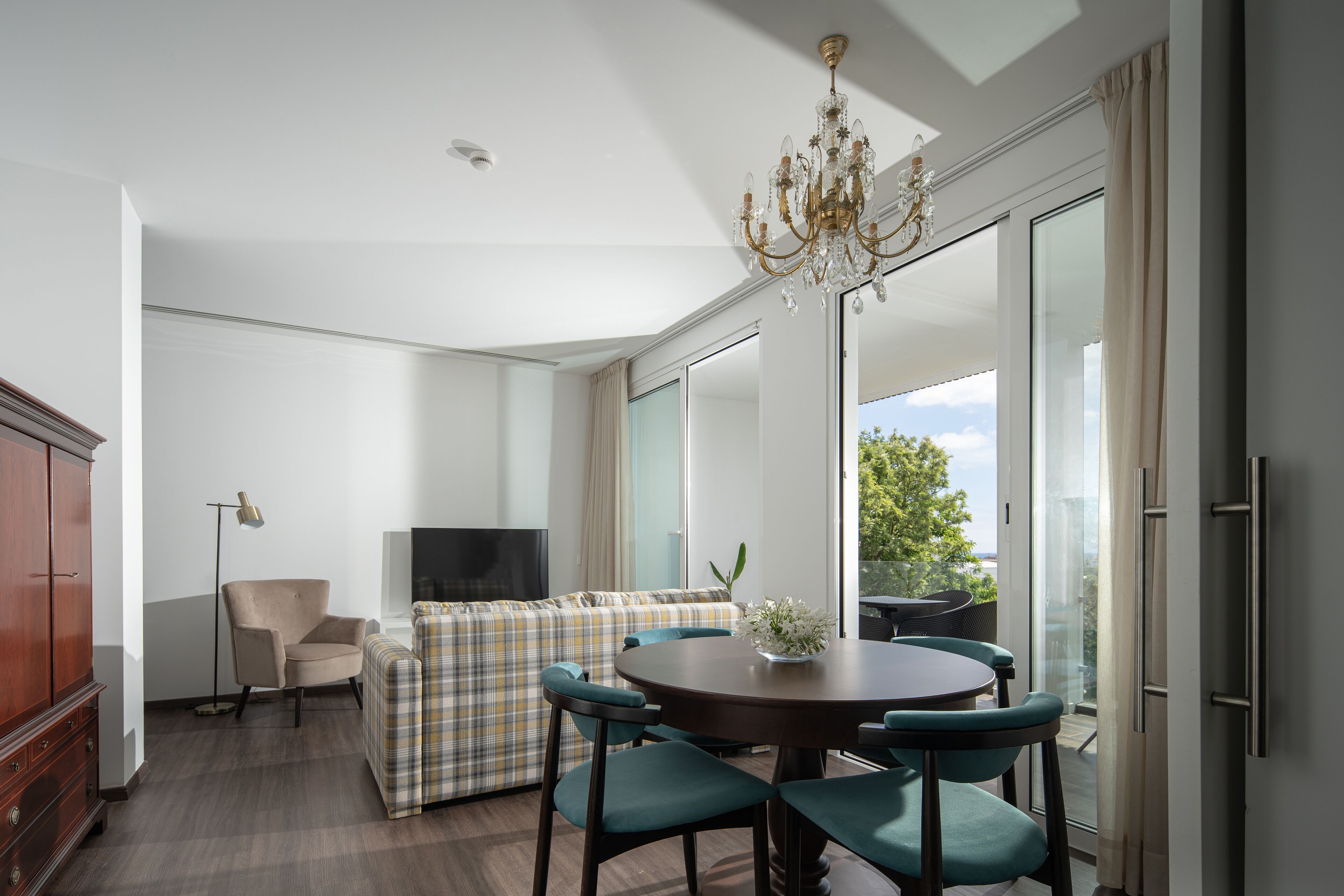 Una sala de estar moderna con un sofá, una mesa de comedor con sillas, una araña y un televisor.