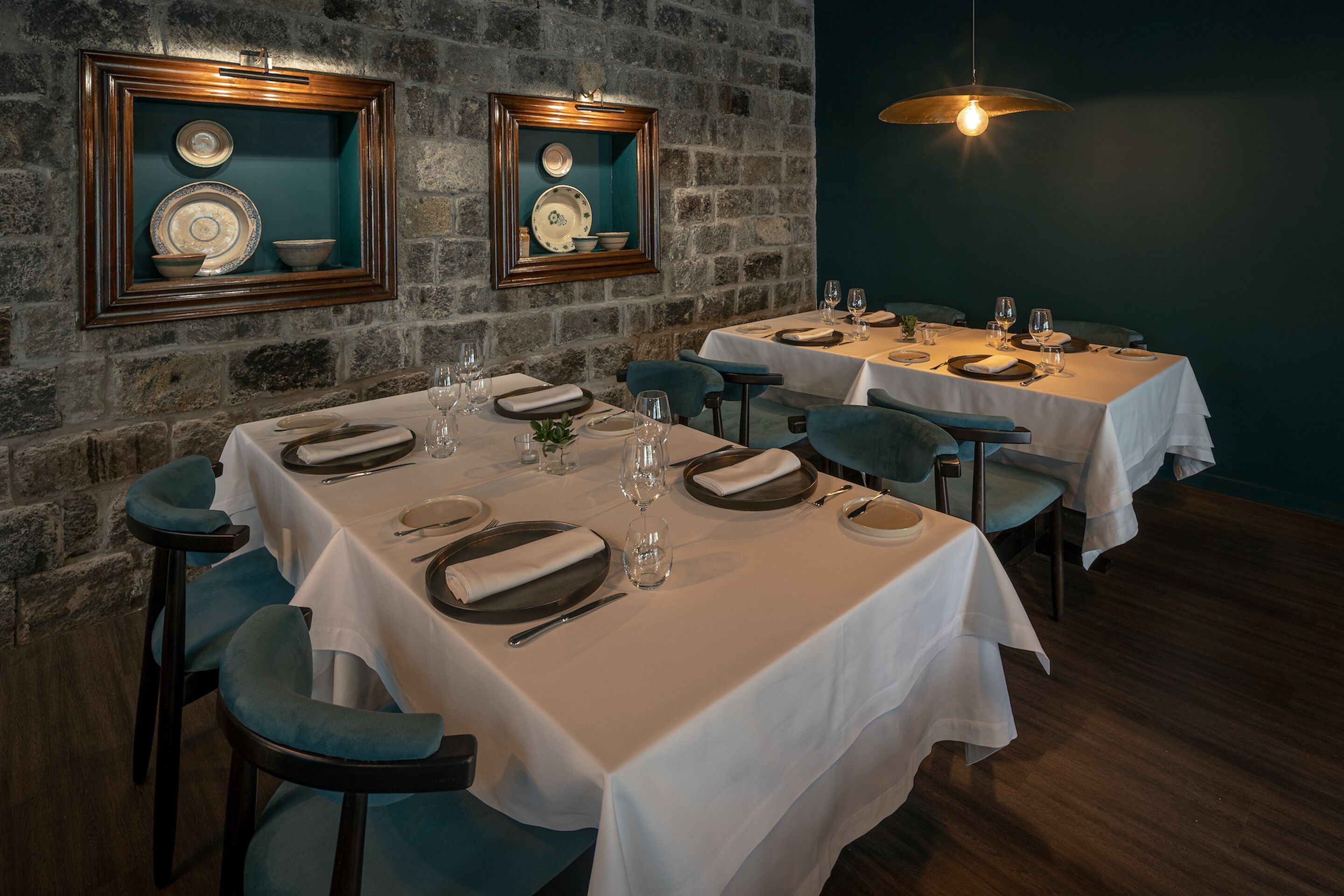 A restaurant with two tables set for dining, each with white tablecloths, plates, and cutlery.